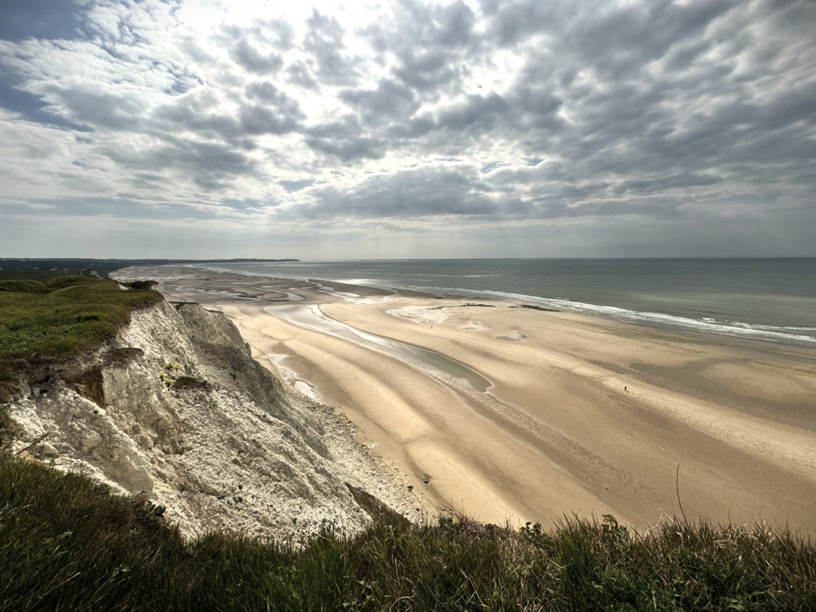 The grass grows fearless at the edge, overlooking the vastness of sea and sky at Normandy